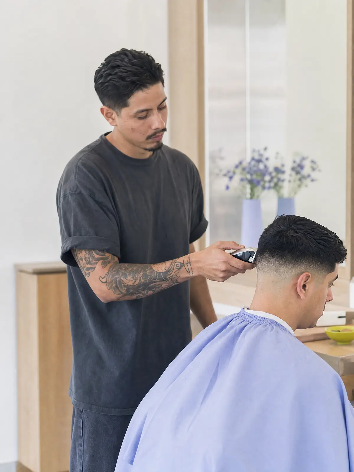 A barber working clippers into a client's fade in a bright modern barbershop
