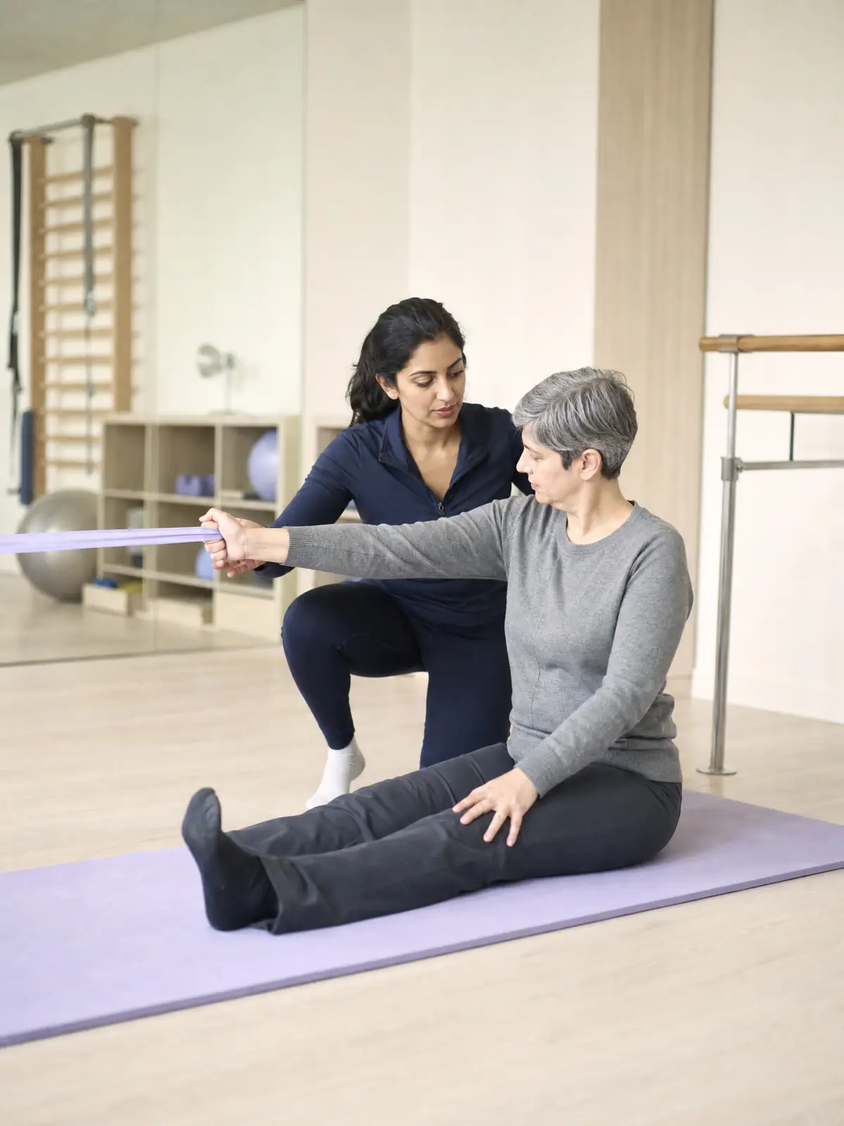 A physiotherapist kneeling beside a seated patient, guiding their arm through a resistance-band exercise